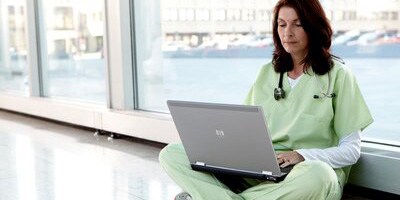 Ärztin sitzt auf dem Boden und schaut auf ihren Laptop
