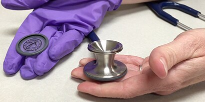 Hände, die das Bruststück eines 3M™ Littmann® Classic III™ Stethoskops mit austauschbarer einteiliger Membran halten.
