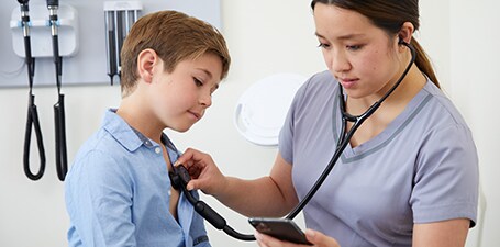 Arzt, der den Brustkorb eines Jungen auskultiert, während er auf eine Smartphone-App schaut
