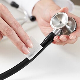 Hände wischen mit einem Alkoholtupfer den Schlauch eines Littmann Stethoskops ab.